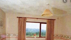 A hotel room with a bed, a desk, a chair, a window with curtains, and a hanging light fixture. - Scottshotel (Pontypridd)
