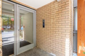 A hotel entrance with a glass door, a brick wall, and a no-smoking sign. - Gold Rush Apartments (Cambridge)