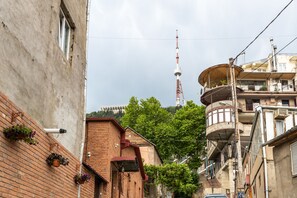A narrow urban street with brick buildings, a tower in the background, and balconies with potted plants. - 4 keys (Tbilisi)