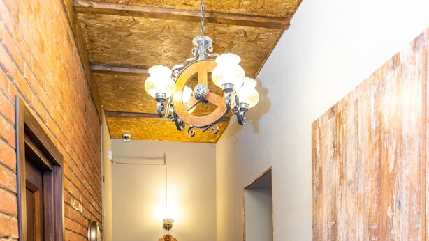 Ein Flur mit Holzboden, Backsteinwänden und einer Holztür. Zwei orangefarbene Stühle und ein Blumentopf sind ebenfalls zu sehen.