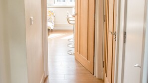A narrow hallway with wooden flooring leading to a room with a window and a chair. - LUXURIOUS penthouse HEART of Cambridge (Cambridge)