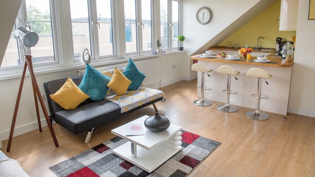A modern living room with a sofa, coffee table, and a dining area with bar stools. - LUXURIOUS penthouse HEART of Cambridge (Cambridge)