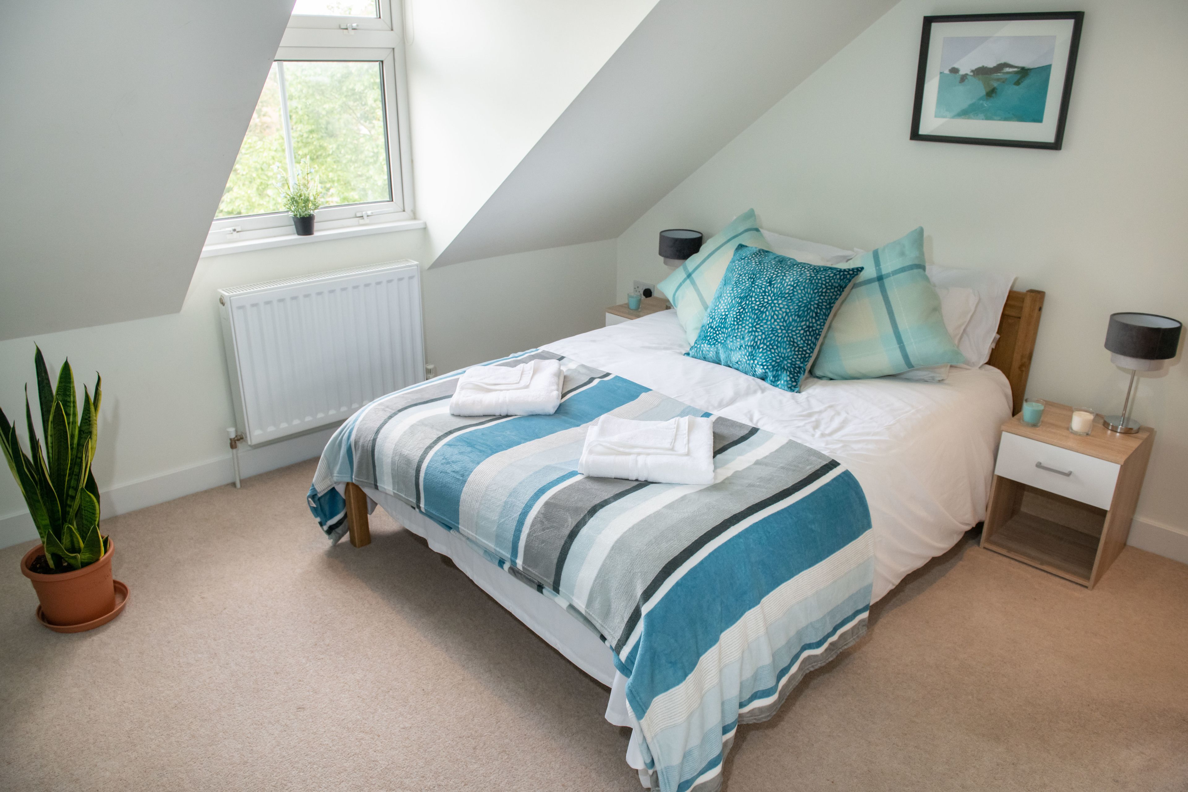 A bedroom with a bed, nightstands, a potted plant, a radiator, and a window.