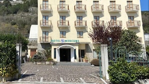 A multi-story hotel with a central entrance, balconies on each floor, and a stone pathway leading to the entrance. - Hotel Mercure (Castelluccio Inferiore)