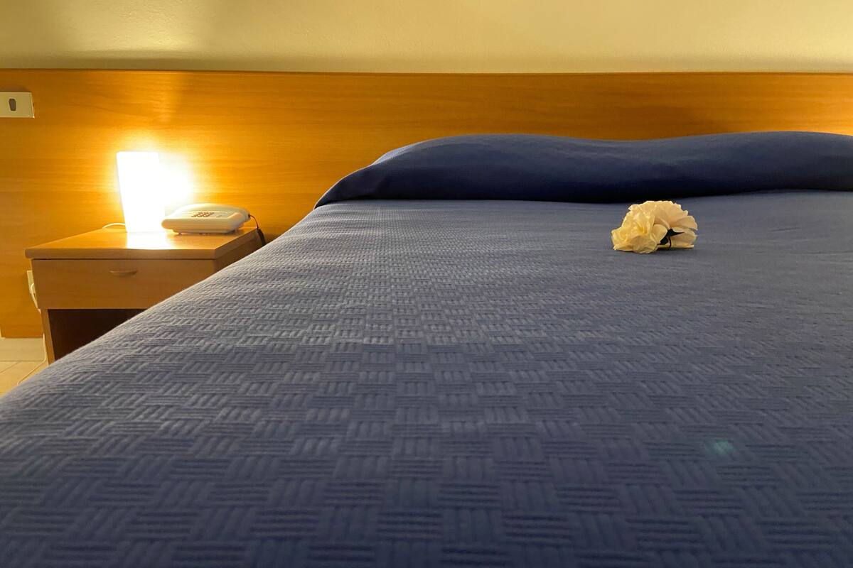 Un lit bien fait, avec une couverture bleue à motifs et un seul objet décoratif posé sur l’oreiller.