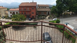 A residential area with a red building, a parking lot, and a street. - Hotel Mercure (Castelluccio Inferiore)