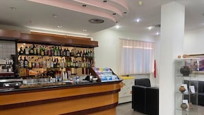 A reception area with a wooden counter, a display of liquor bottles, a coffee machine, and a seating area with a glass display case. - Hotel Mercure (Castelluccio Inferiore)