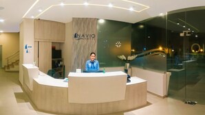 Una recepción con diseño moderno, una recepcionista y el logotipo de NAVIO HOTEL.