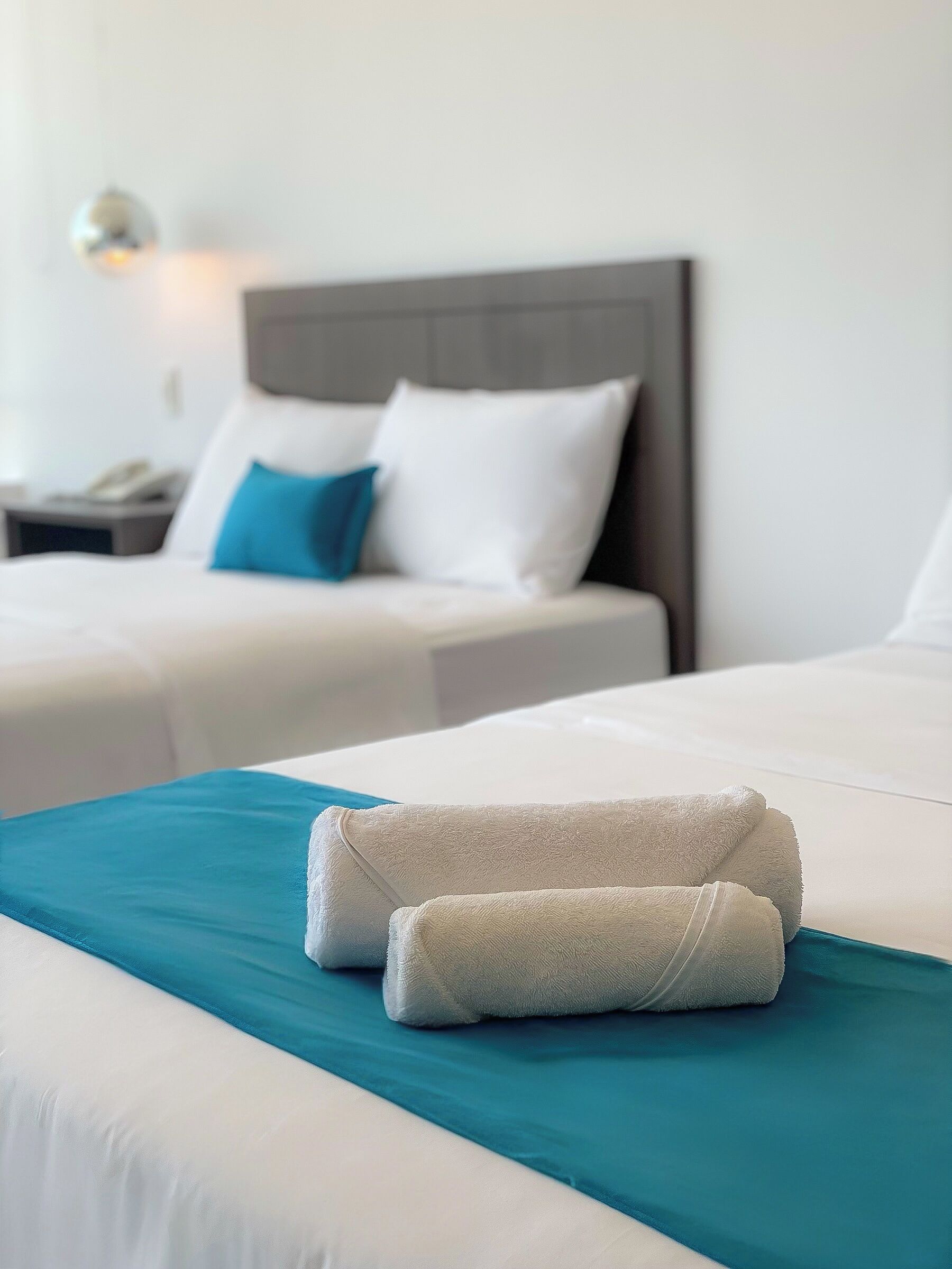 A hotel room with two beds, each with white linens and a teal accent.