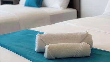 A hotel room with two beds, each with white linens and a teal accent.