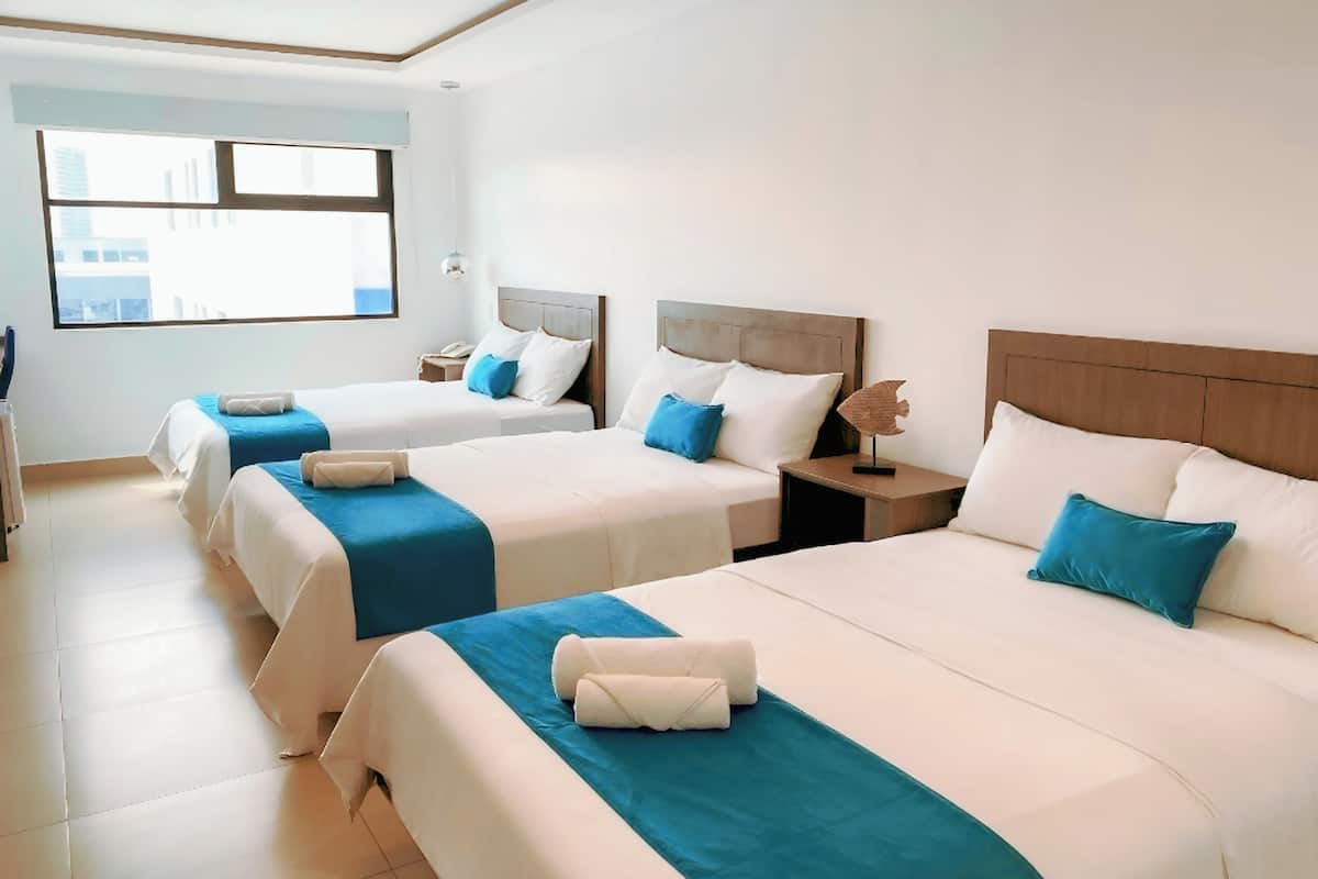 A hotel room with two beds, each with a blue bedspread and white pillows, and a wooden headboard. There is a nightstand with a lamp and a decorative fish sculpture.