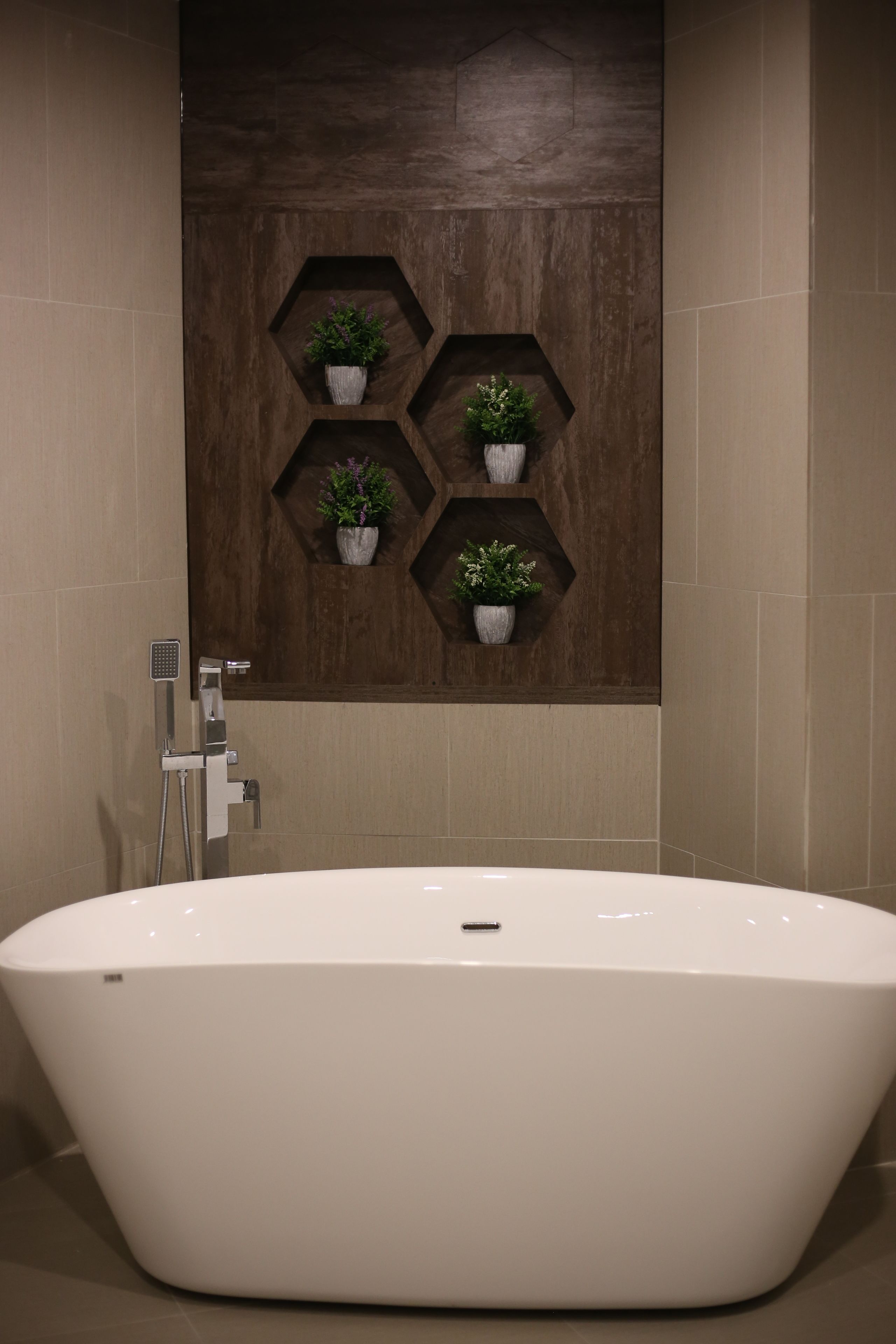A modern bathroom with a freestanding bathtub, hexagonal shelving with potted plants, and a shower area with a handheld showerhead.
