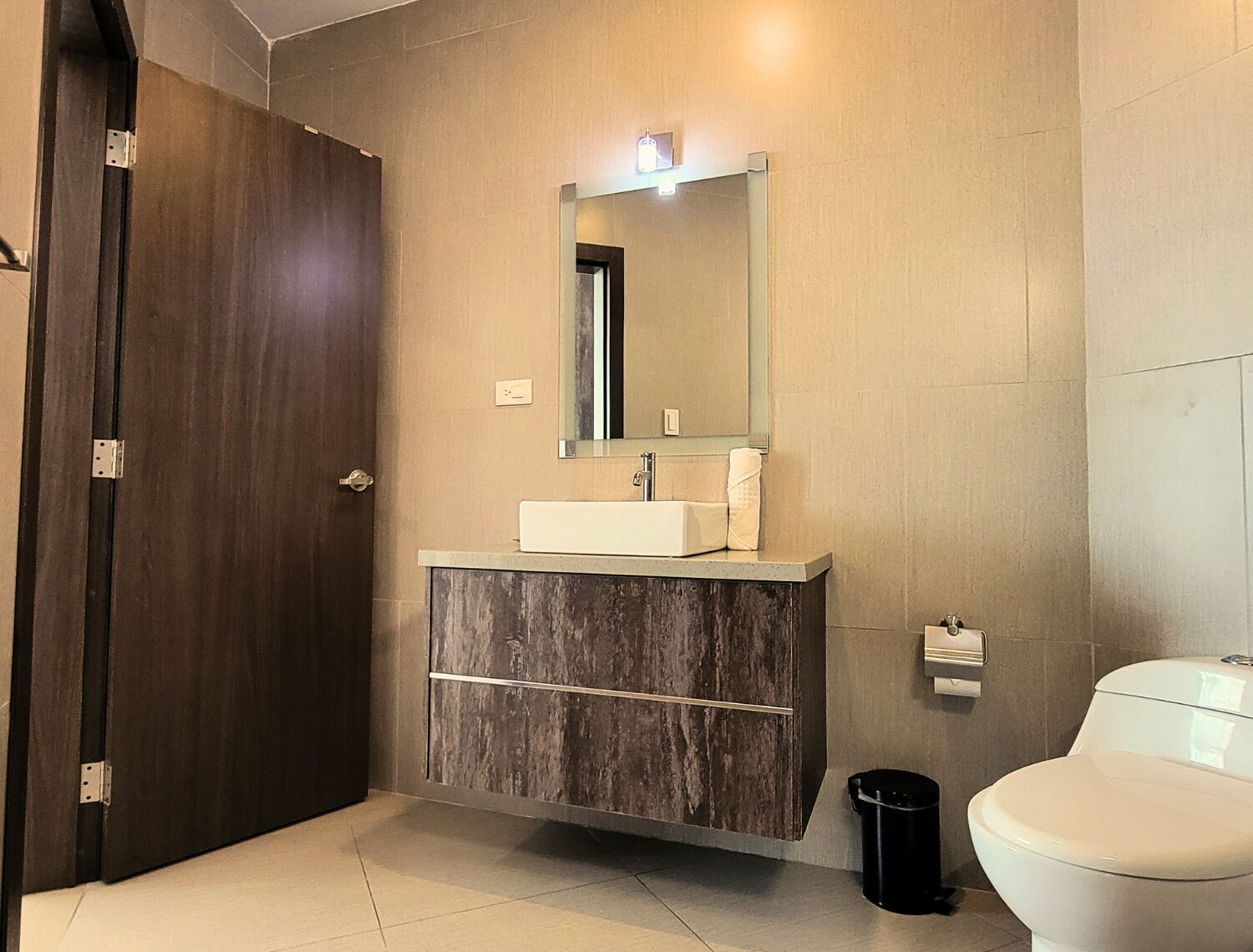 A modern bathroom with a dark wood door, a white sink with a mirror above it, and a toilet.
