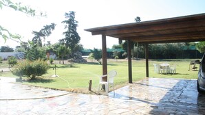 An outdoor patio area with stone flooring, a covered seating area, and a grassy lawn. - Casa Anna (Quartu Sant'Elena)