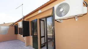 Un edificio residencial con un patio empedrado, una puerta corrediza de vidrio y un equipo de aire acondicionado blanco montado en la pared exterior.