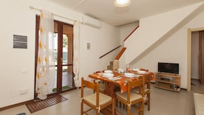 Un comedor con una mesa dispuesta para cuatro personas, un televisor sobre un mueble bajo y una escalera que sube a otro nivel.