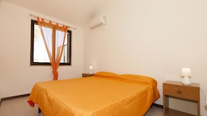 Un dormitorio con cama, mesita de noche, aire acondicionado y ventana con cortinas.