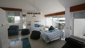 Ein Zimmer mit zwei Betten, einem Schlafsofa und einem Sessel. Es gibt Fenster und eine Tür.