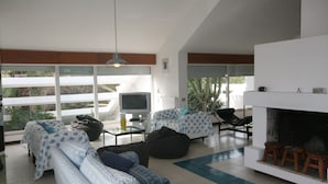 Ein modernes Wohnzimmer mit einer Sofagarnitur, einem Fernseher, einem Kamin und Blick ins Freie.