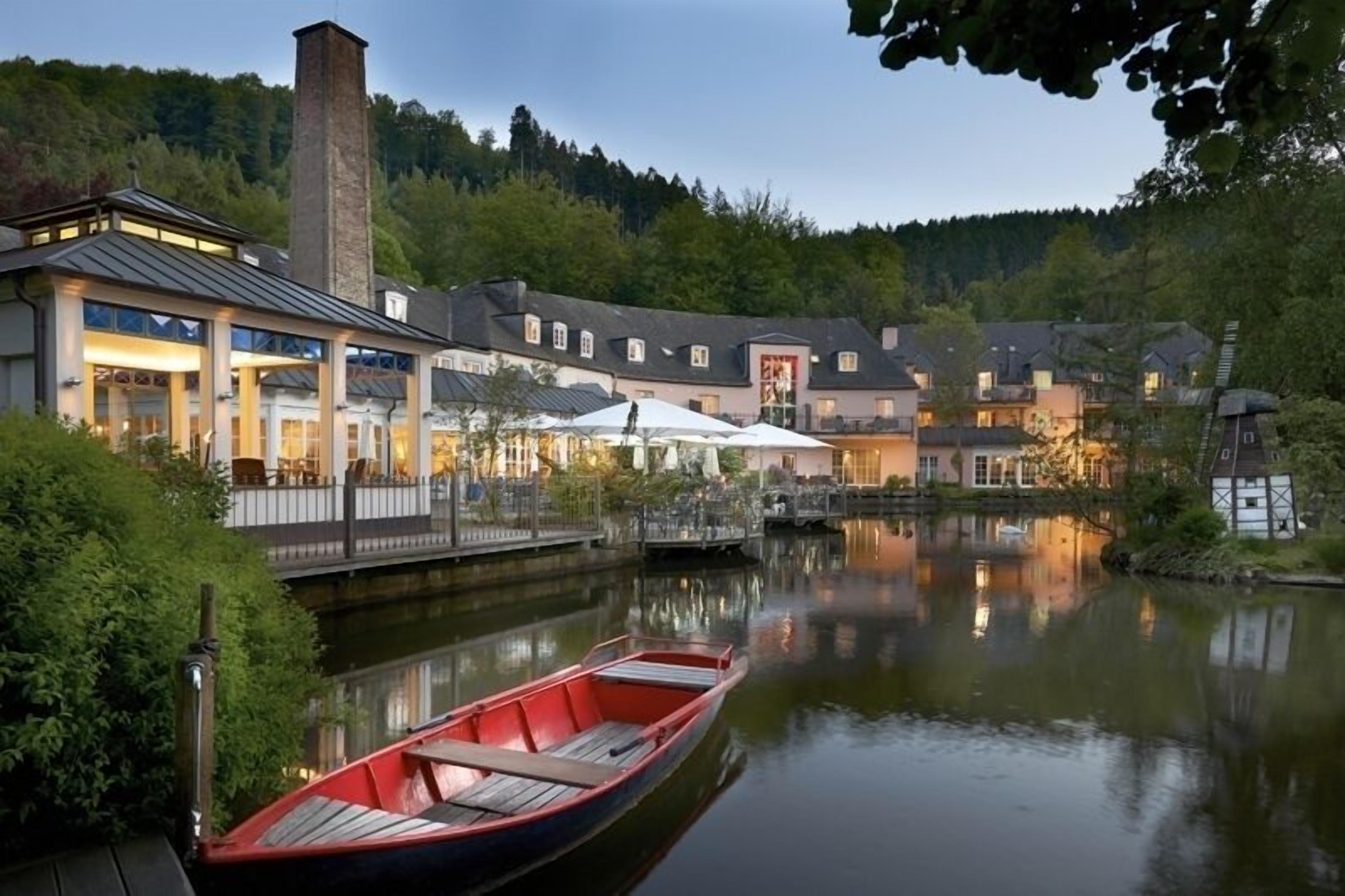 Een hotel aan de rivier met een steiger, een boot en een brug naar de gebouwen.