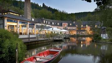 Een hotel aan de rivier met een steiger, een boot en een brug naar de gebouwen.
