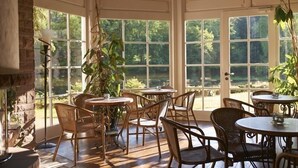 A sunlit room with large windows, wicker furniture, and a stone wall. - Hotel Molitors Mühle (Eisenschmitt)