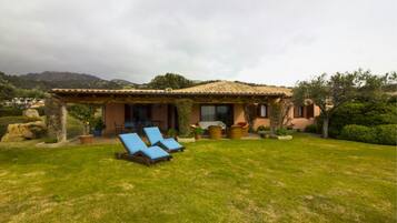 Una casa con un patio, dos sillones azules y un jardín.