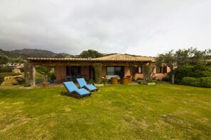 A house with a patio, two blue lounge chairs, and a garden.