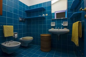 A bathroom with blue tiles, a white sink, a bidet, a toilet, and a yellow towel.