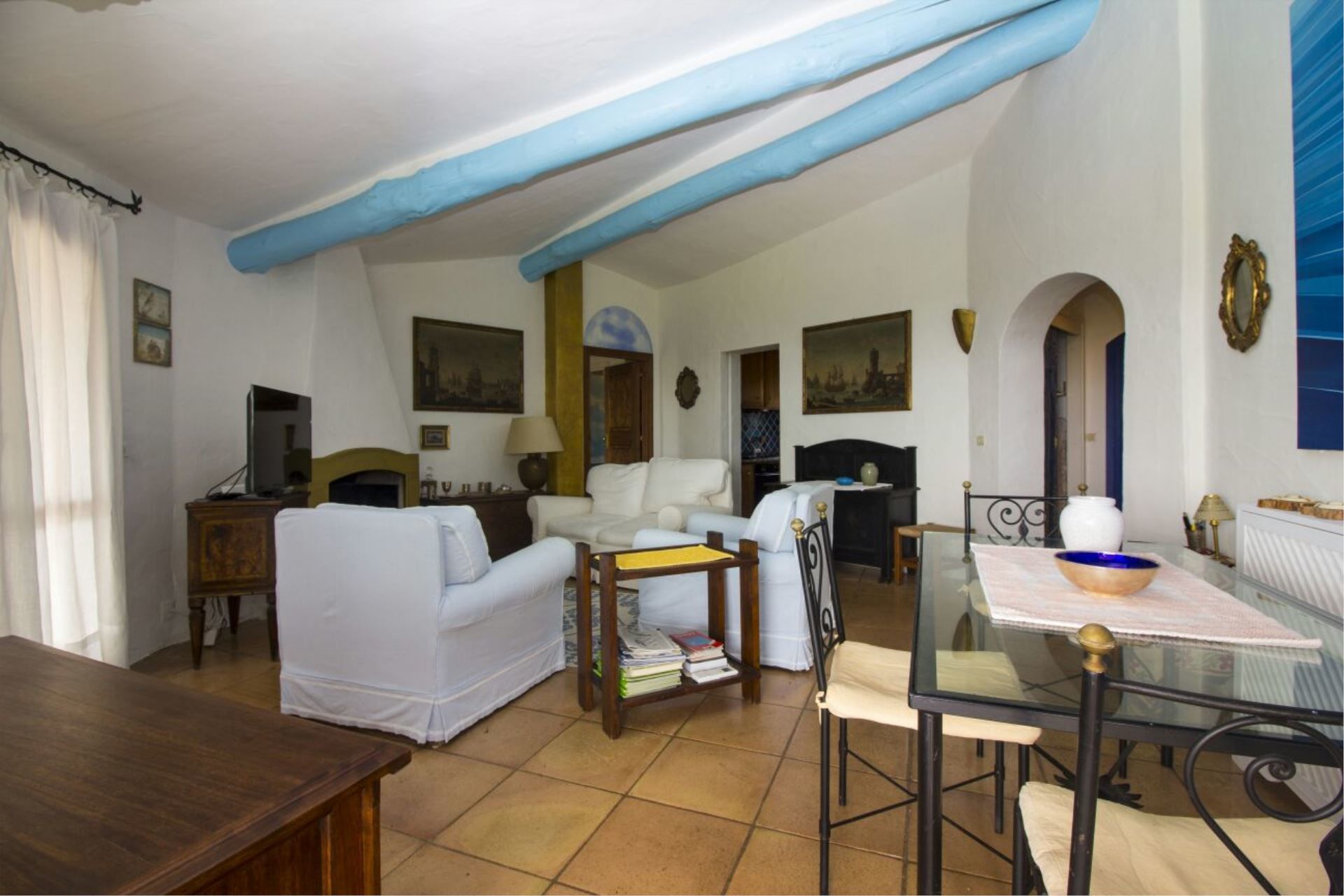 A spacious living room with a high ceiling, white sofas, a glass table, and a fireplace.