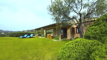 Una villa con porche cubierto, césped y vistas del paisaje circundante.
