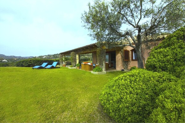 A villa with a covered patio, a grassy lawn, and a view of the surrounding landscape.