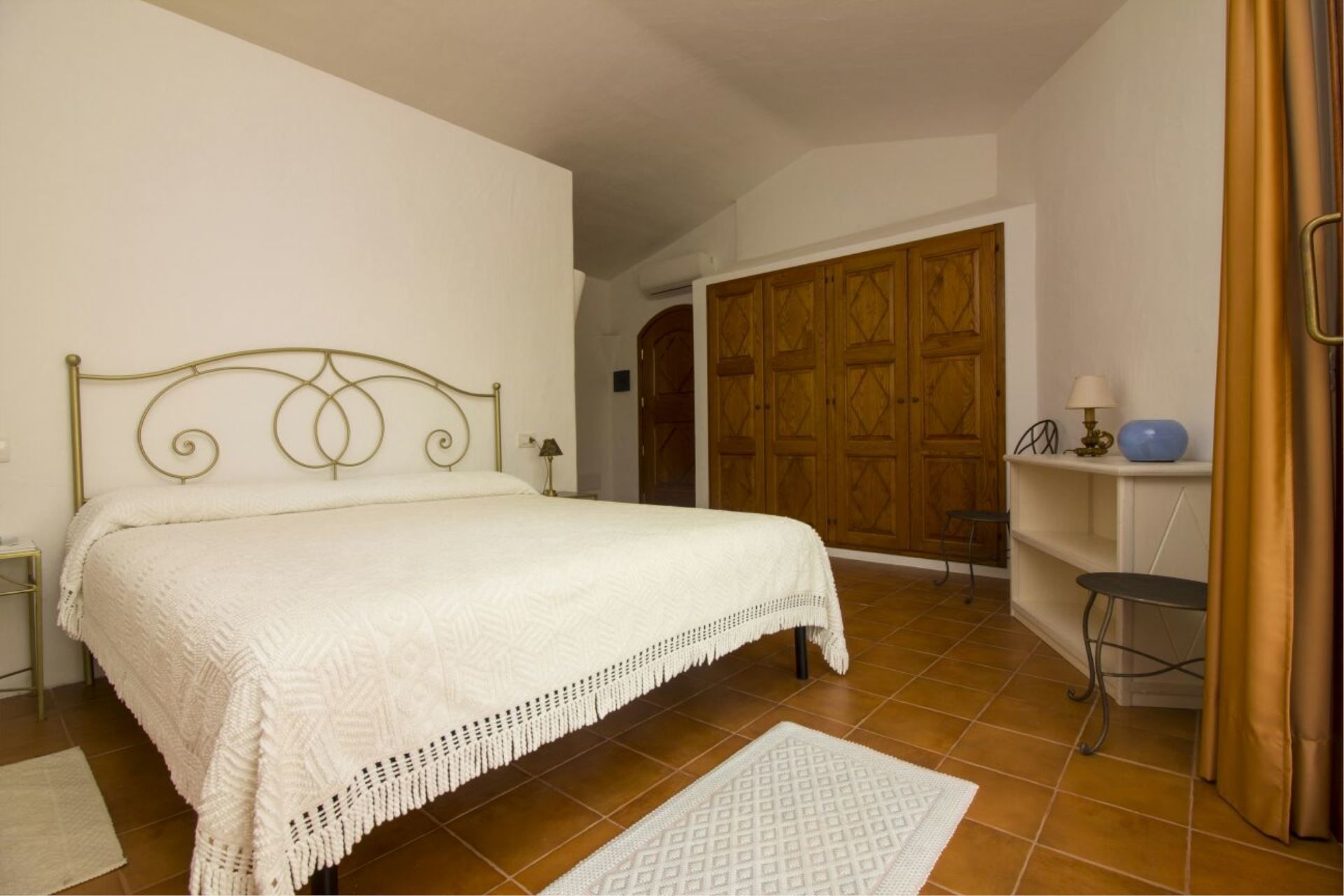 A bedroom with a bed, a nightstand, a lamp, a chair, a wardrobe, and a bathroom area.
