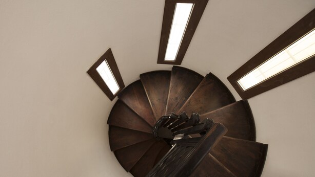 Una escalera de caracol con escalones de madera y barandilla metálica, que asciende.