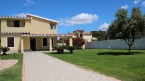 Una casa de dos pisos con un patio empedrado que conduce a la entrada, rodeada por un césped cuidado y algunos árboles.