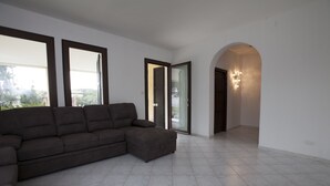 Una sala de estar moderna con un sofá seccional, ventanas amplias y un pasillo que lleva a una puerta con una lámpara.