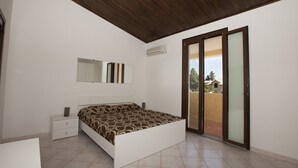 Un dormitorio con cama, mesita de noche, espejo y puerta corrediza de vidrio que da a un área exterior.
