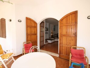Ein Zimmer mit einem weißen runden Tisch, zwei Korbstühlen mit roten Kissen und einer Holztür, die in einen anderen Raum führt.