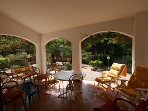 Eine überdachte Terrasse mit rundem Tisch und Stühlen, umgeben von Bögen.