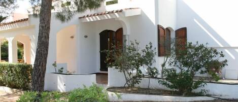 A white building with a tiled roof, a tree, and a garden area with a circular planter.