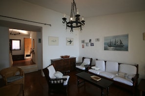 A living room with a sofa, chairs, a coffee table, and a chandelier. There are wall decorations and a door leading to another room.