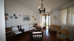A spacious living room with a high ceiling, a chandelier, a sofa, a dining table, and wicker furniture. - Villa Gianina (Maracalagonis)