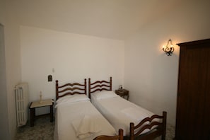 A bedroom with two wooden beds, a nightstand, a wall-mounted light fixture, and a radiator.