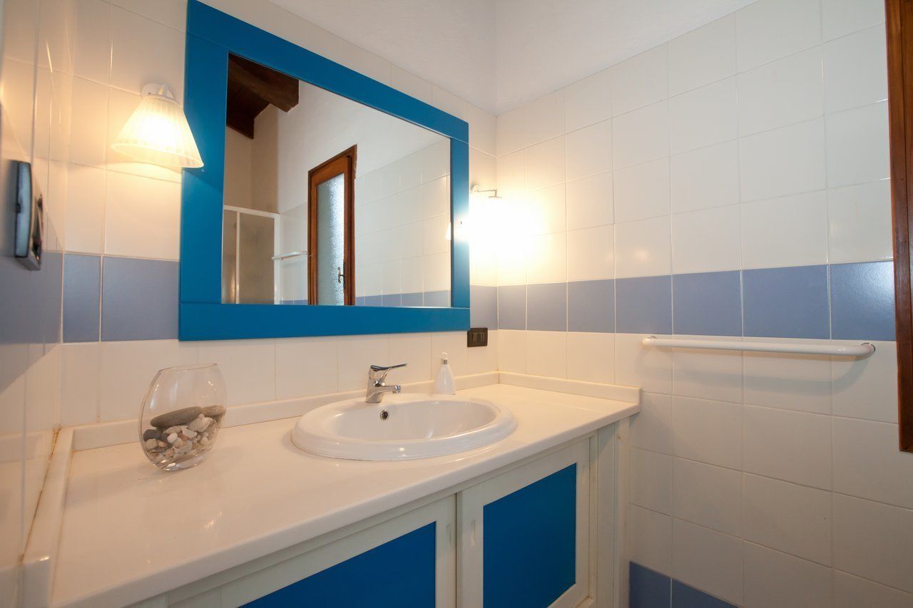 Une salle de bain avec un lavabo blanc, des murs recouverts de carreaux bleus, un miroir et un porte-serviettes.