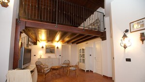 Un salón amplio con techo alto, vigas de madera, un balcón y un comedor.