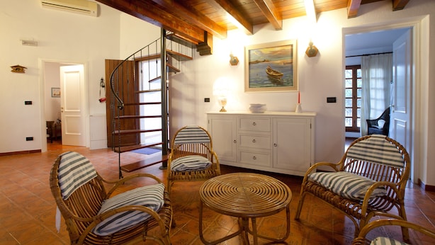 Un amplio salón con muebles de mimbre, una escalera de madera y un cuadro en la pared.