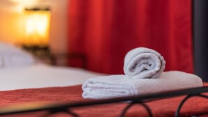 Une serviette blanche, soigneusement pliée, est posée sur un couvre-lit rouge dans une chambre d’hôtel.