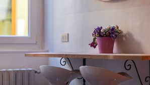 Une pièce avec une étagère en bois sur laquelle est posé un pot rose contenant des fleurs violettes, un radiateur blanc et un miroir incurvé accroché au mur.