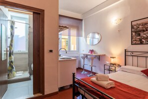 Une chambre à coucher comprenant un lit, une table de chevet, un miroir, une fenêtre et une salle de bain avec une douche et un lavabo.