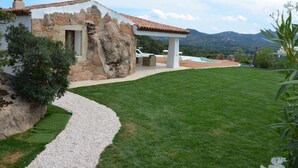 A stone house with a tiled roof, a grassy lawn, and a pool. - Villa La Mendula (Arzachena)